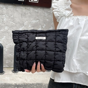 Detail of black quilted puffer cosmetic bag with May Rabbit label held by model