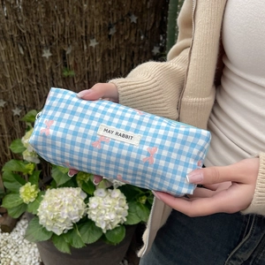 Blue plaid makeup bag with pink bow patterns and white logo tag held by a hand