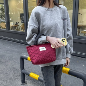 Detail of burgundy quilted tote bag with heart pattern and contrast black handles