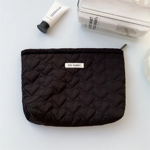Detail shot of black heart-quilted toiletry bag with zipper and logo label