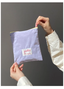 Détail macro d'une trousse à maquillage lilas en nylon plissé avec étiquette brodée