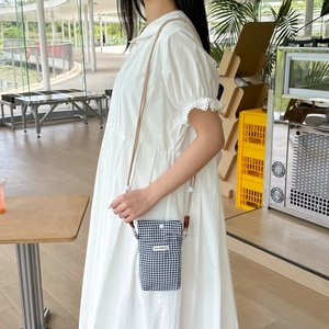 Detail of checkered mobile phone bag with MAY RABBIT label worn over a lace dress