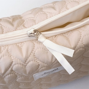 Detail shot of heart quilted texture on beige makeup bag with silk ribbon zipper puller