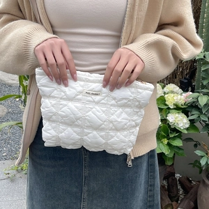 Detail of white quilted cosmetic bag with May Rabbit label held in an outdoor garden
