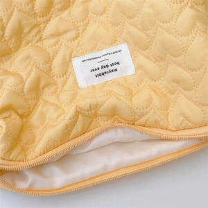 Close-up of quilted heart patterns on yellow makeup bag with woven brand label