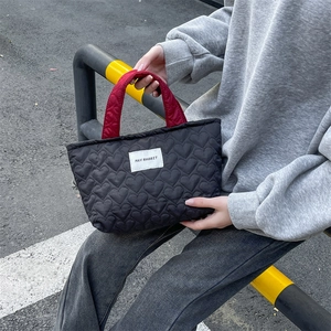 Detail of heart-quilted black tote bag with contrasting burgundy handles and woven brand label