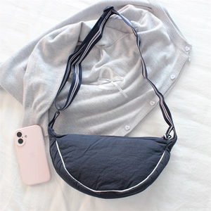 Detail view of navy blue half-moon crossbody bag with striped adjustable strap next to phone