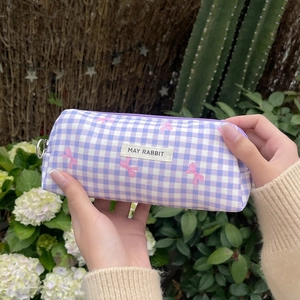 Close-up of checkered makeup bag with bow print and brand label held by hands