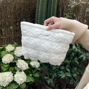 Detail of white quilted nylon makeup bag with gold zipper and MAY RABBIT woven label