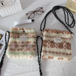 Close-up of striped plush mini crossbody bags with rope straps on a textured fabric