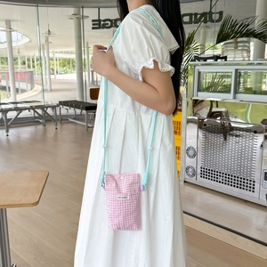 Detailed view of pink plaid crossbody phone bag with light blue woven shoulder strap