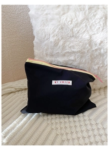 Detail of a black cosmetic bag with pink and yellow zippers and a hi jolly patch
