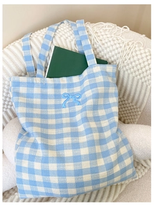 Detailed view of blue plaid canvas tote featuring blue butterfly embroidery on white chair