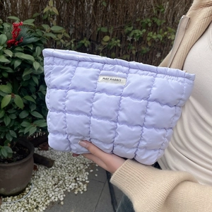 Close-up of a quilted lavender makeup bag featuring a white brand label held by hand