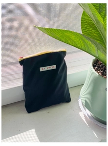 Détail d'une pochette en toile avec fermeture éclair noire et étiquette hi jolls contrastée