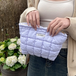 Detail of lavender quilted cosmetic bag with gold zipper held by a model in a garden