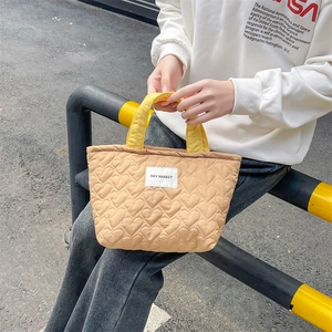 Detail of light tan quilted handbag with heart patterns and yellow handles for women