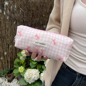 Cute pink plaid cosmetic bag with bow patterns and zipper, held in a garden setting