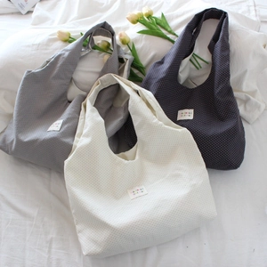 Detailed view of polka dot tote bags in grey, beige and navy blue on a white bed