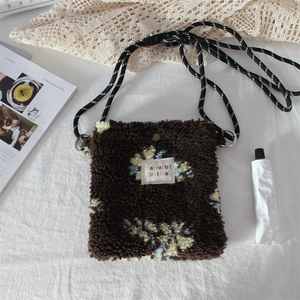 Close-up of brown plush crossbody bag featuring floral patterns and woven strap detail
