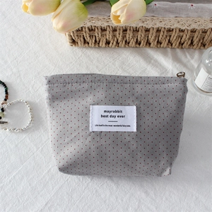 Detailed view of a gray polka dot makeup bag with brand label and metal zipper