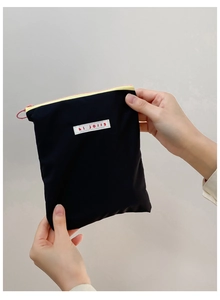 Détail d'une pochette en tissu noir avec zip jaune et étiquette blanche hi jolly