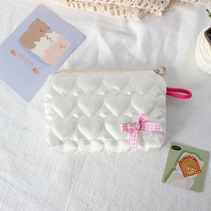 Detail of white heart-quilted storage pouch with pink bow and satin finish texture