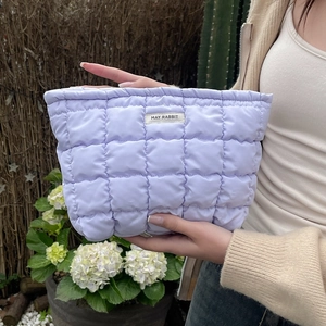Close-up of light purple quilted cosmetic bag held by hands in an outdoor setting