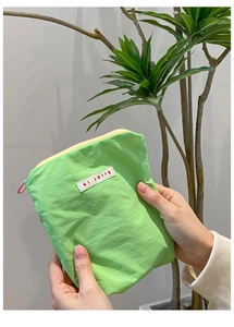 Détail d'une pochette en nylon vert clair montrant le tissu texturé et le zip coloré