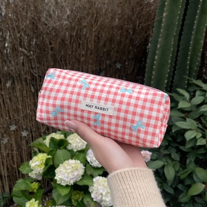 Pink checkered pencil case with blue bow prints and woven label in an outdoor garden