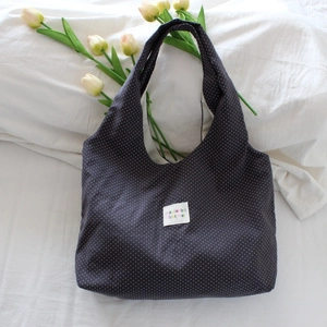 Detail of navy blue polka dot canvas tote bag featuring a white woven label on bed linens