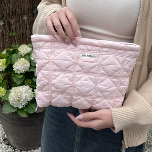 Quilted pink makeup bag with diamond stitching held by a person outdoors