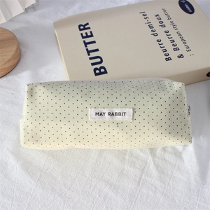 Detailed top view of a cream canvas pencil case with green polka dots on white fabric