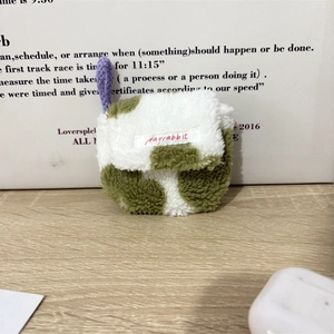 Detail van pluche oortelefoonhoesje met groene koeienprint en paars gevlochten koord