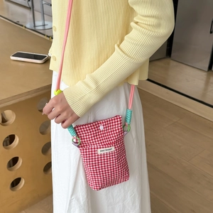 Close-up of red and white checkered crossbody phone bag with pink braided strap and label