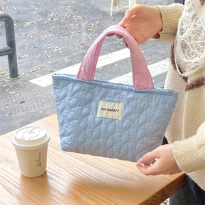 Detail of blue quilted tote bag with pink handles and heart stitching in outdoor setting