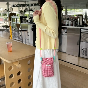 Close-up of red plaid fabric crossbody phone bag with pink rope strap and logo detail