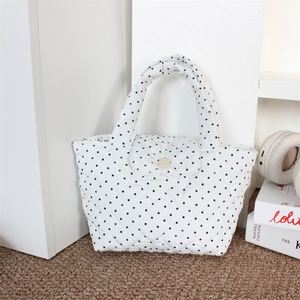 Close-up of white heart-quilted handbag with black polka dots and gold buckle closure