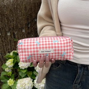 Detailed close-up of a pink plaid cosmetic bag with blue bow patterns and logo label