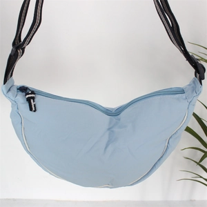 Close-up of light blue nylon crescent bag with adjustable striped strap and white piping