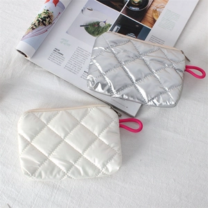 Quilted silver and beige makeup bags with bright pink wristlet handles on a magazine