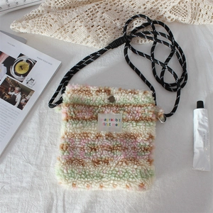 Close-up of plush crossbody bag in pink and green faux fur on white fabric background