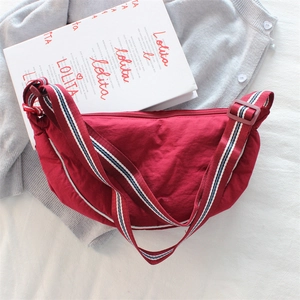 Close-up of red nylon crescent bag with adjustable multicolor striped strap and zipper detail