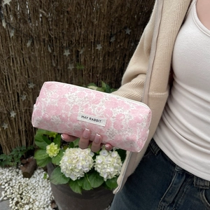 Close-up of pink floral canvas makeup bag with woven label held by a hand