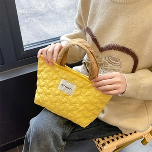 Detail of yellow heart-quilted handbag with brand label and stitched handles