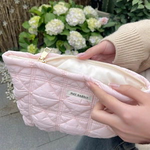 Detailed view of hand opening a quilted pink cosmetic bag with gold zipper and woven label
