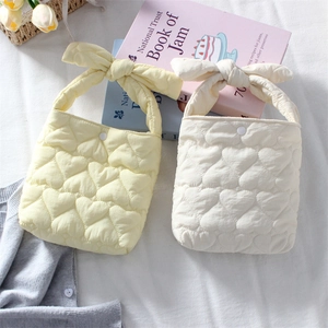 Quilted heart handbags with bow handles in cream and white displayed on a soft fabric base