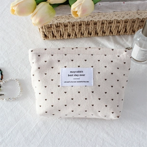 Detailed close-up of cream canvas makeup bag with heart patterns and zip closure