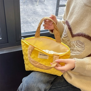 Detail of yellow quilted handbag with heart patterns, zip closure and khaki strap handles