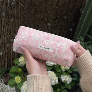 Pink floral zipper storage bag with brand label held in a natural outdoor garden setting
